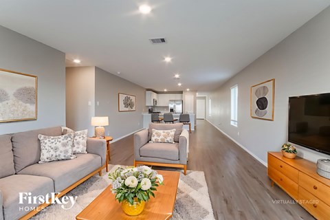 A living room with a grey couch, a coffee table with flowers, and a flat screen TV.