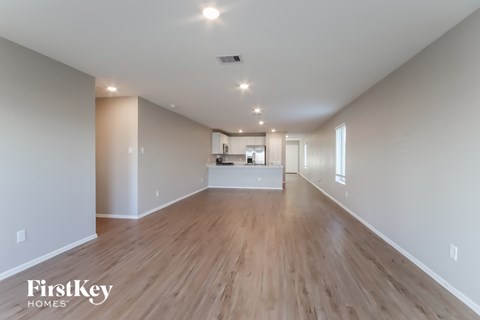 A spacious room with wooden floors and a kitchen area in the background.