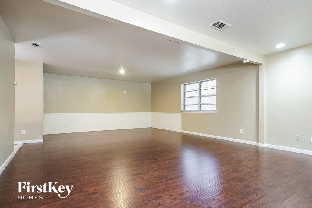 A spacious room with wooden floors and a window on the wall.