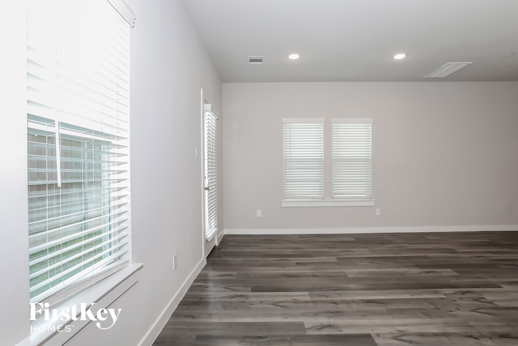 A room with wooden flooring and two windows with blinds.