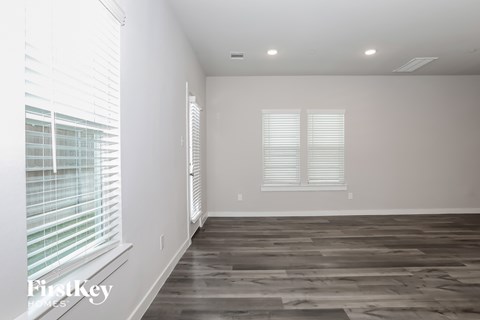 A room with wooden flooring and two windows with blinds.