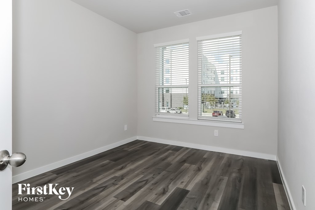 A room with wooden flooring and a view of a street through the window.