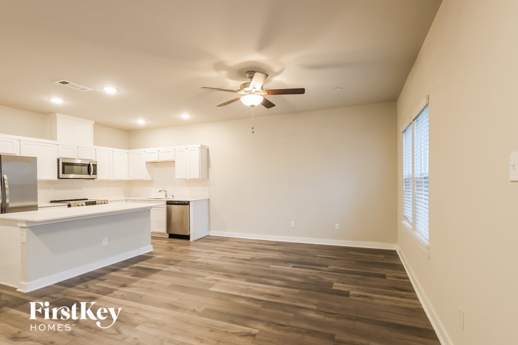 A spacious kitchen and living room with wooden floors and a ceiling fan.