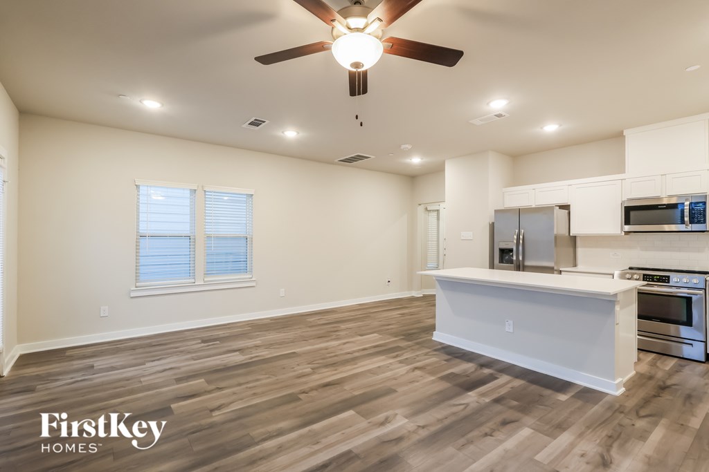 A spacious kitchen with a wooden floor and a ceiling fan.