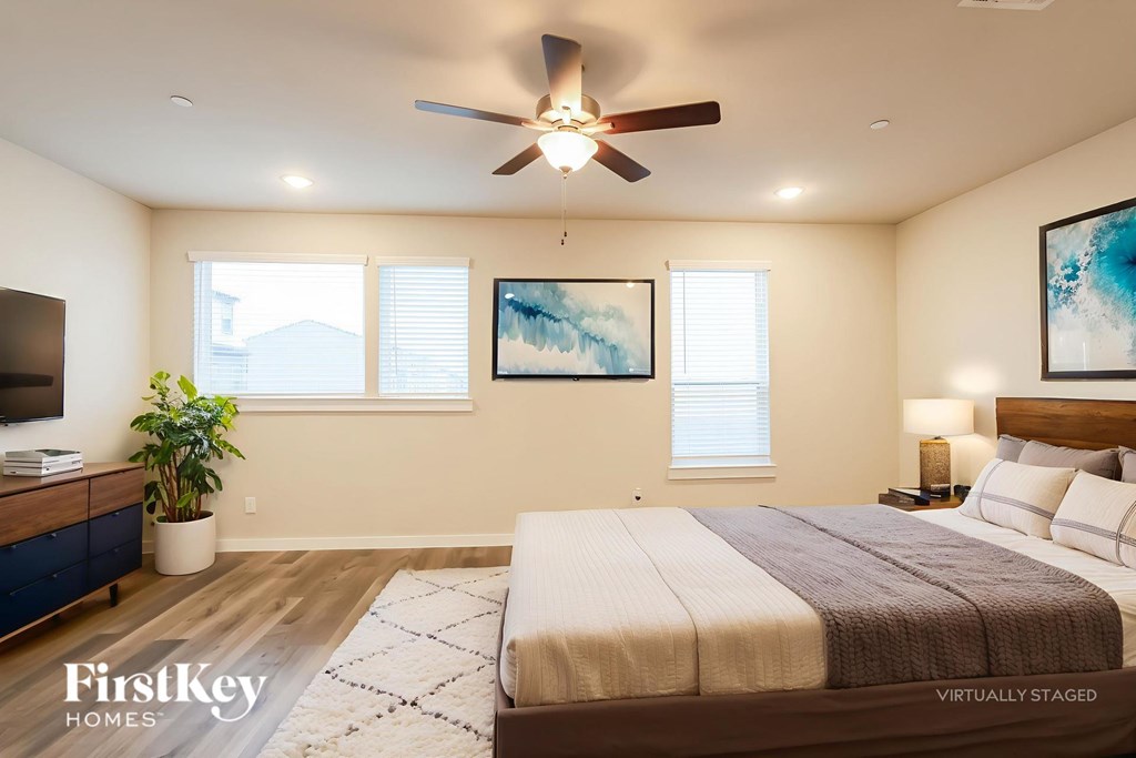 A bedroom with a bed, a ceiling fan, and a painting on the wall.