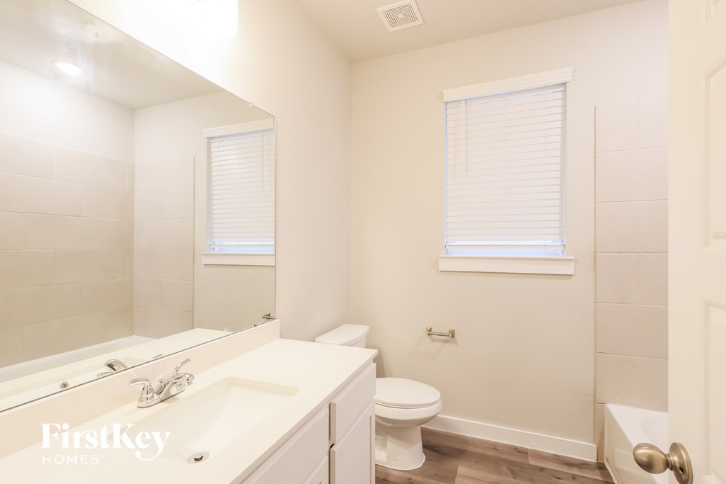 A white bathroom with a mirror, sink, toilet and tub.
