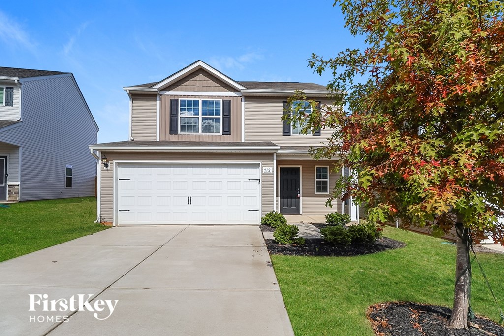 A house with a garage and a tree in front of it.