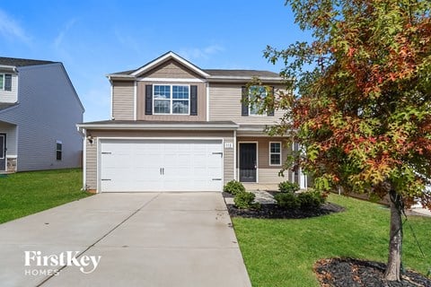A house with a garage and a tree in front of it.