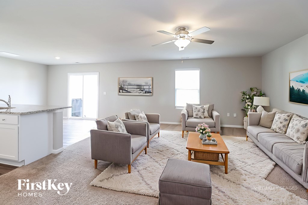 A well-lit living room with a grey sofa, a grey armchair, a grey ottoman, a wooden coffee table, and a painting on the wall.