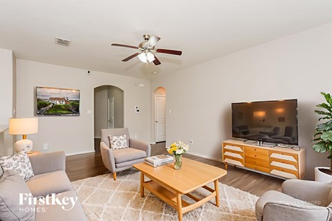 A living room with a grey couch, a wooden coffee table, a flat screen TV and a ceiling fan.
