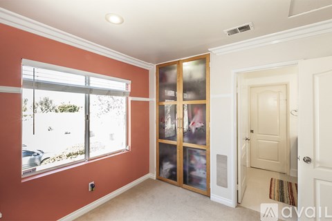 A room with orange walls and a large window with a view of trees and a car.