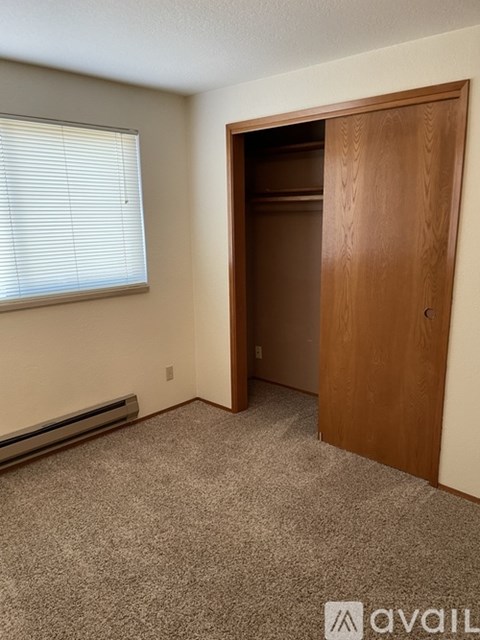 A room with a carpeted floor, a window with blinds, a wooden door, and a wall-mounted air conditioner.
