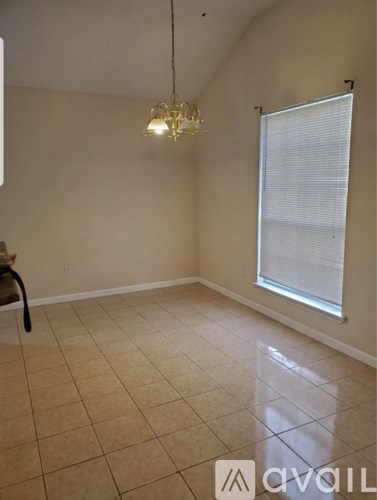 A room with a chandelier, a window with blinds, and a chair.