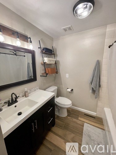 A bathroom with a white sink, toilet, and a shower with a grey towel hanging on the wall.