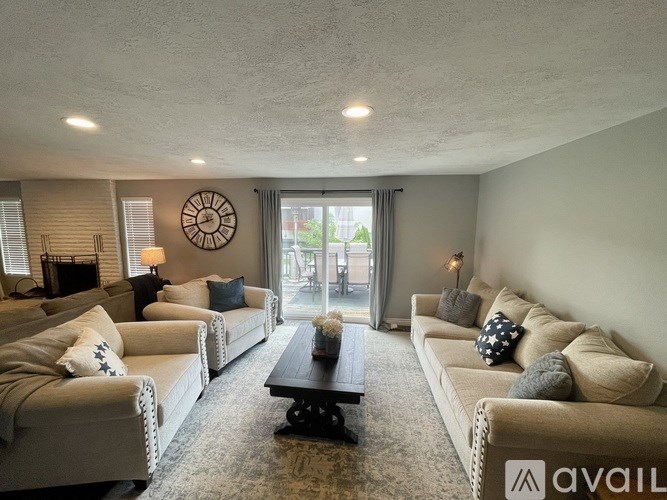 A living room with a large clock on the wall and a couch with a blue pillow.