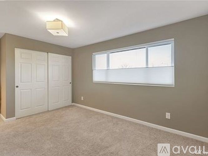 A room with a carpeted floor, a window with blinds, and a ceiling light fixture.