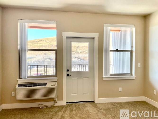 A room with a door, a window with a view of a parking lot, and a window with blinds.