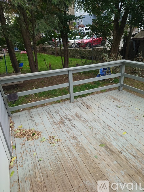 A wooden deck with a white railing and fallen leaves on it.