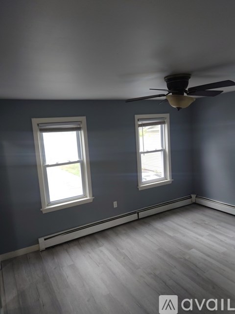 A room with a ceiling fan and two windows.