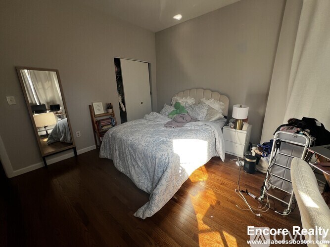 A bedroom with a bed, chair, and mirror.