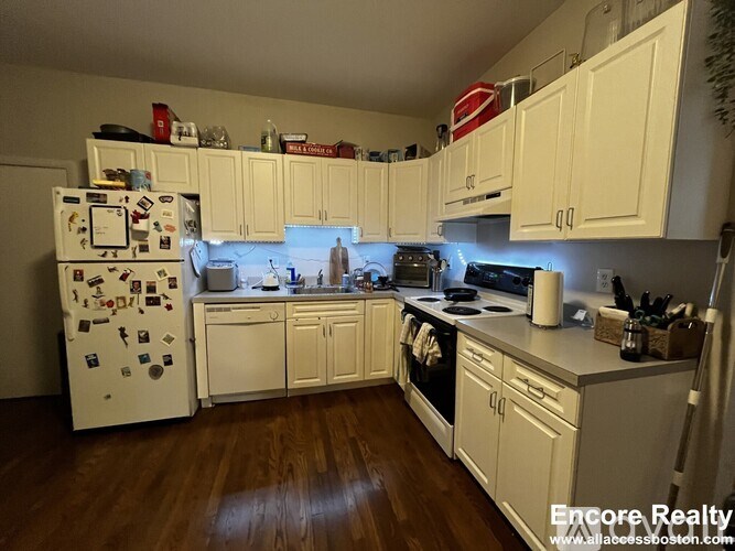 A kitchen with white cabinets and a white fridge with many magnets on it.