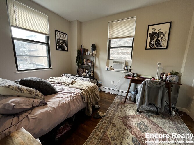 A bedroom with a bed, a desk, and a window.