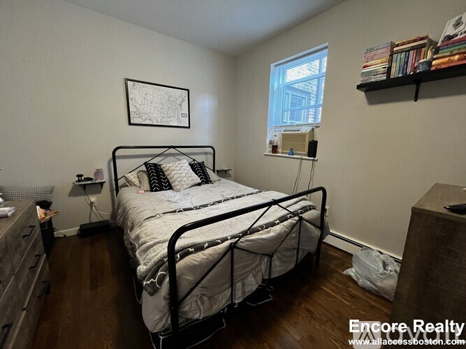 A bedroom with a bed, a nightstand, a lamp, and a window.