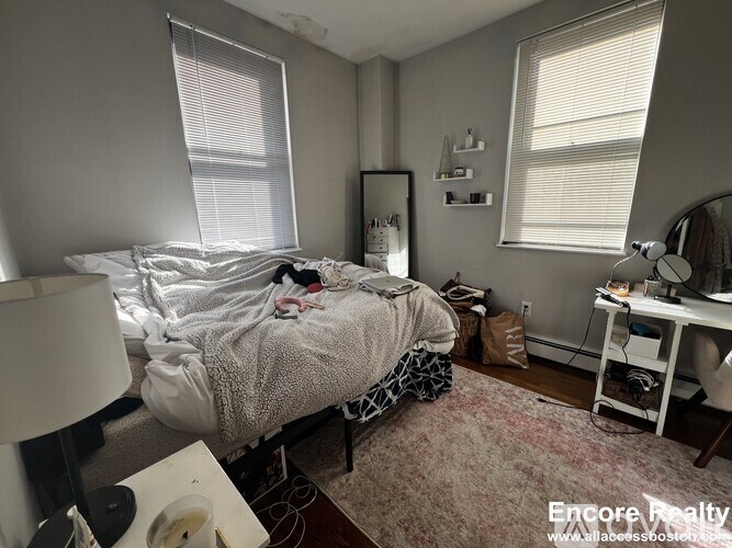 A messy bedroom with a bed, desk, and window.
