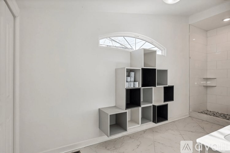 A bathroom with a white tiled floor and a white shelving unit with black cubes.