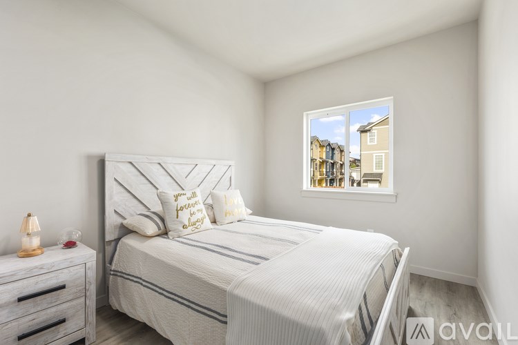 A bedroom with a bed, nightstand, and a window showing a view of houses.