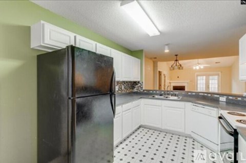 A black refrigerator in a kitchen with white cabinets and a black and white floor.
