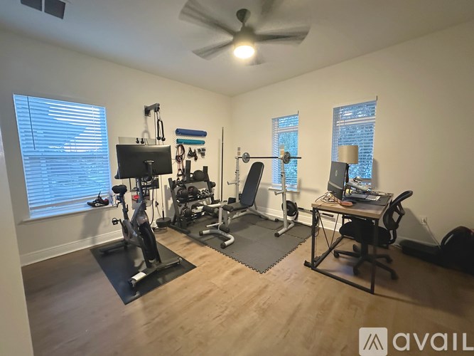 A room with a treadmill, exercise equipment, a desk, and a fan.