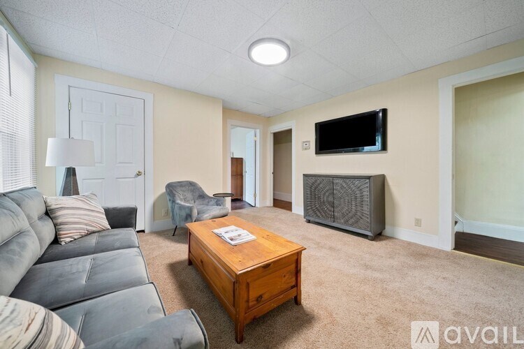 A living room with a grey couch, a wooden coffee table, and a flat screen TV mounted on the wall.