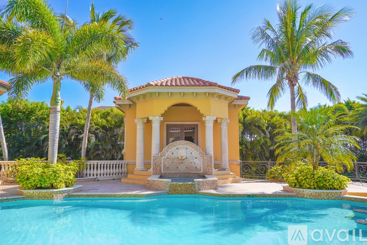 A pool in front of a yellow building with palm trees around it.