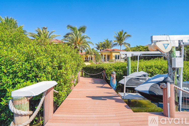 A wooden walkway leads to a dock with boats and a building in the background.