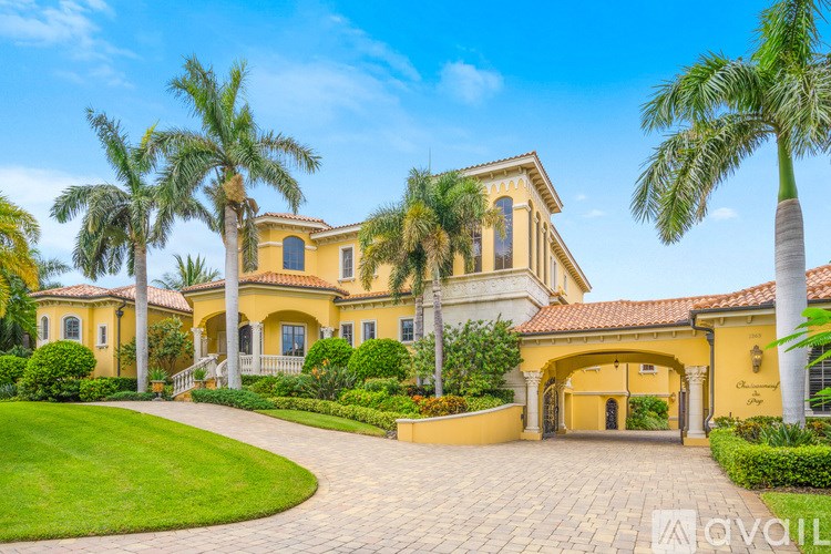 A large, yellow house with a red tile roof and a driveway leading to the front door.