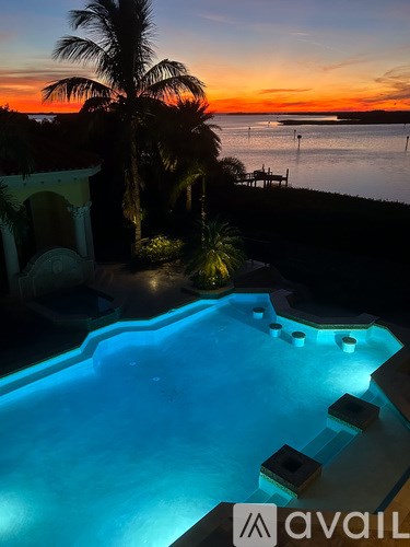 A pool with a sunset in the background and palm trees.
