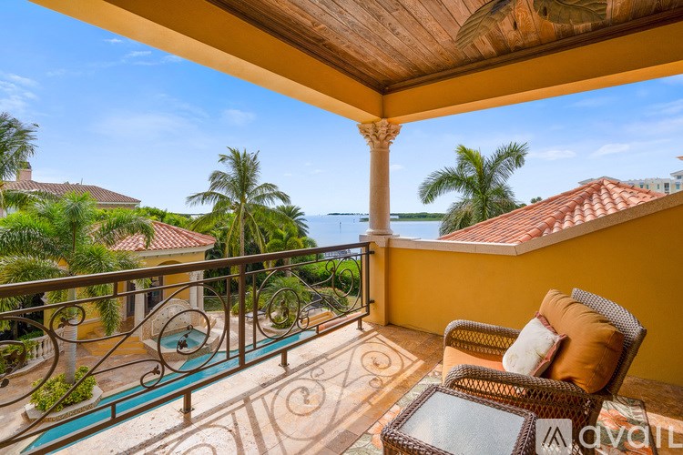 A balcony with a chair and a table overlooking a pool and palm trees.
