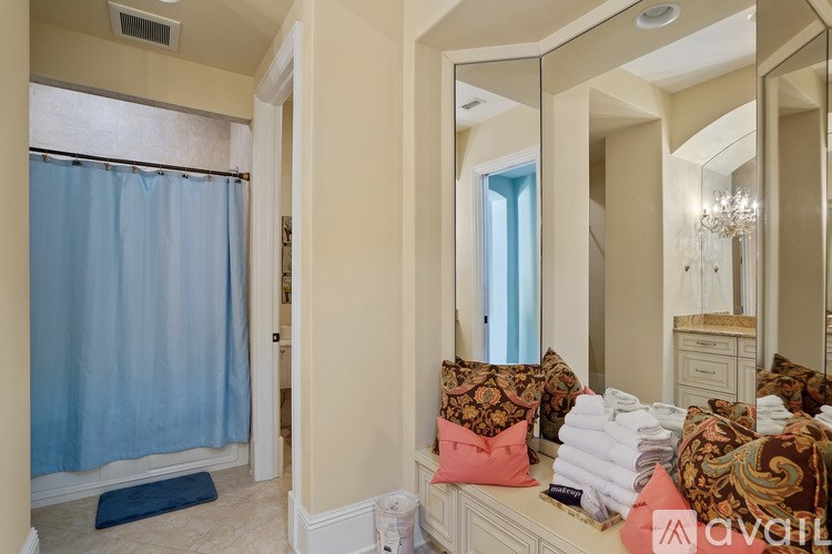 A bathroom with a blue shower curtain and a mirror above a bench with towels on it.