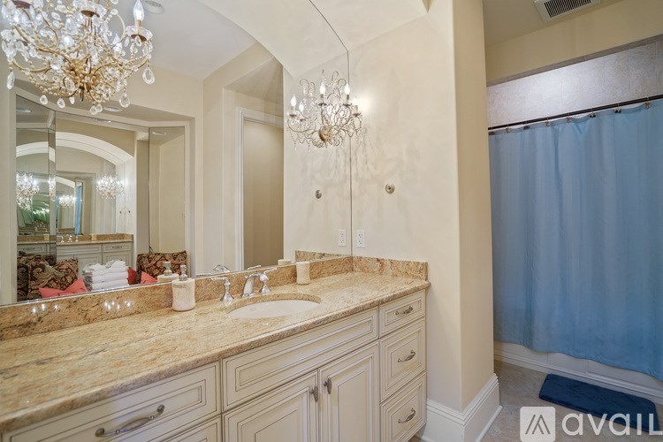 A bathroom with a chandelier, a mirror, a sink, and a shower curtain.