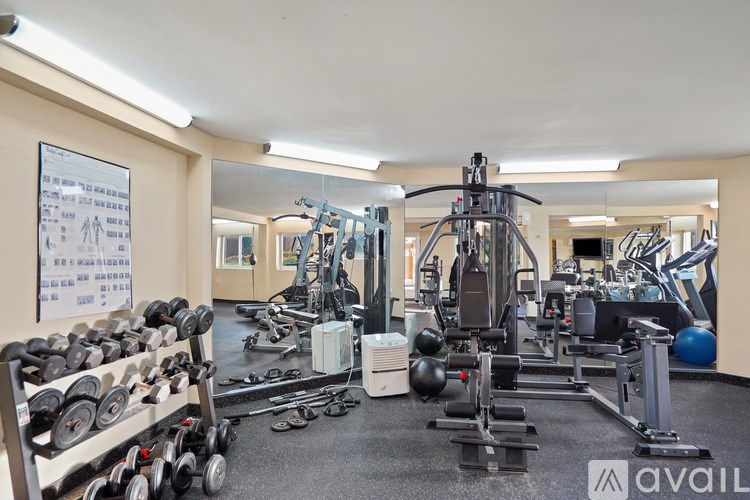 A gym with a variety of equipment including dumbbells, weight plates, and a leg press machine.