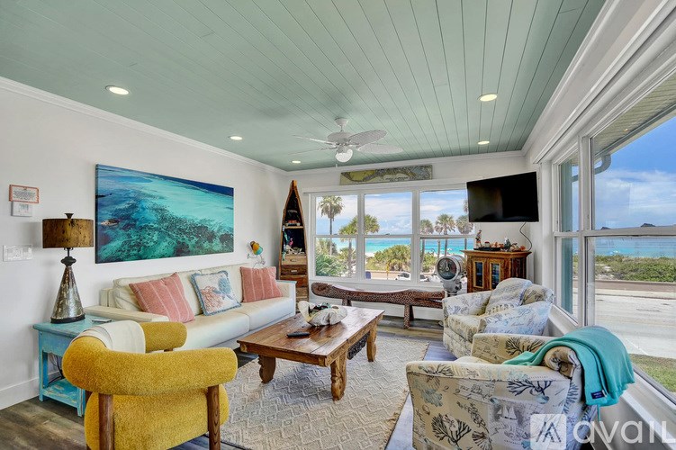 A living room with a yellow chair and a painting of a beach scene on the wall.