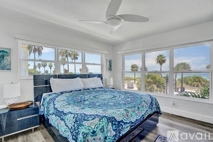 A bedroom with a bed, a ceiling fan, and a view of palm trees through the windows.