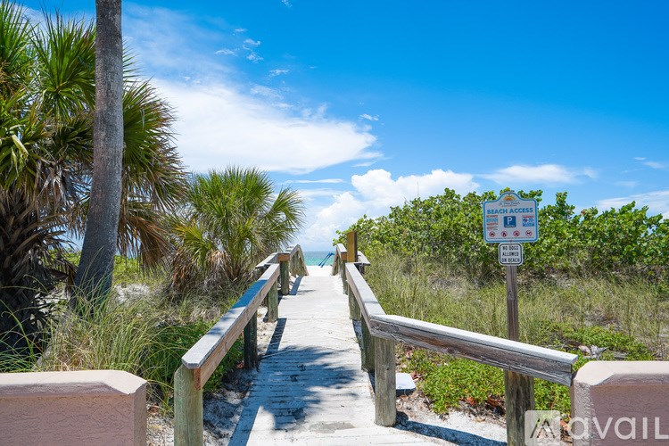 A wooden walkway with a railing leads to a beach.