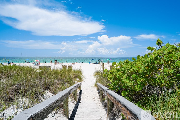 A wooden walkway leads to a beach with people and umbrellas in the distance.