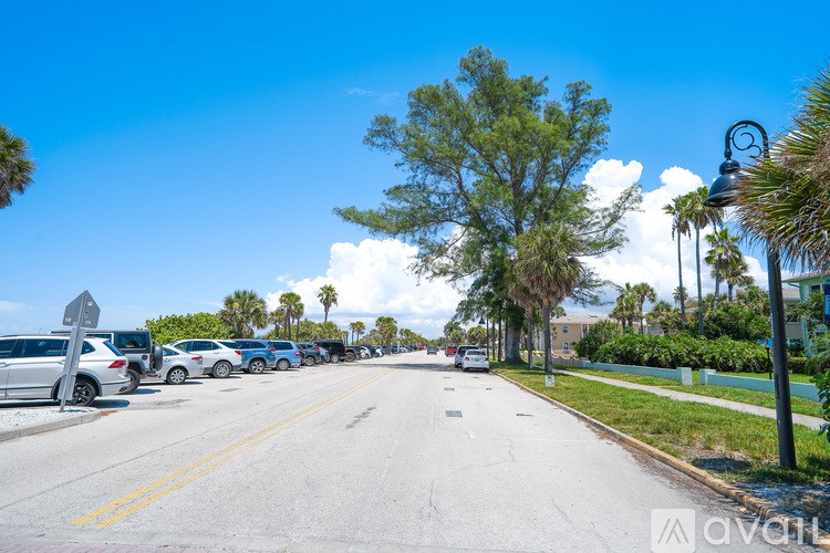 A street with cars parked on the side and palm trees lining the road.
