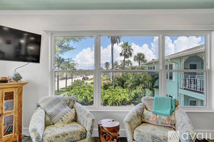 A living room with a large window overlooking a street with palm trees.