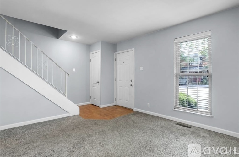 A room with a carpeted floor, a window with blinds, and a white door.