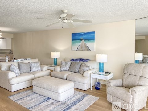 A living room with a white couch, a white chair, a white ottoman, and a painting on the wall.