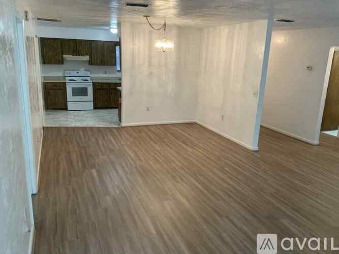 A room with wooden flooring and a kitchen area in the background.